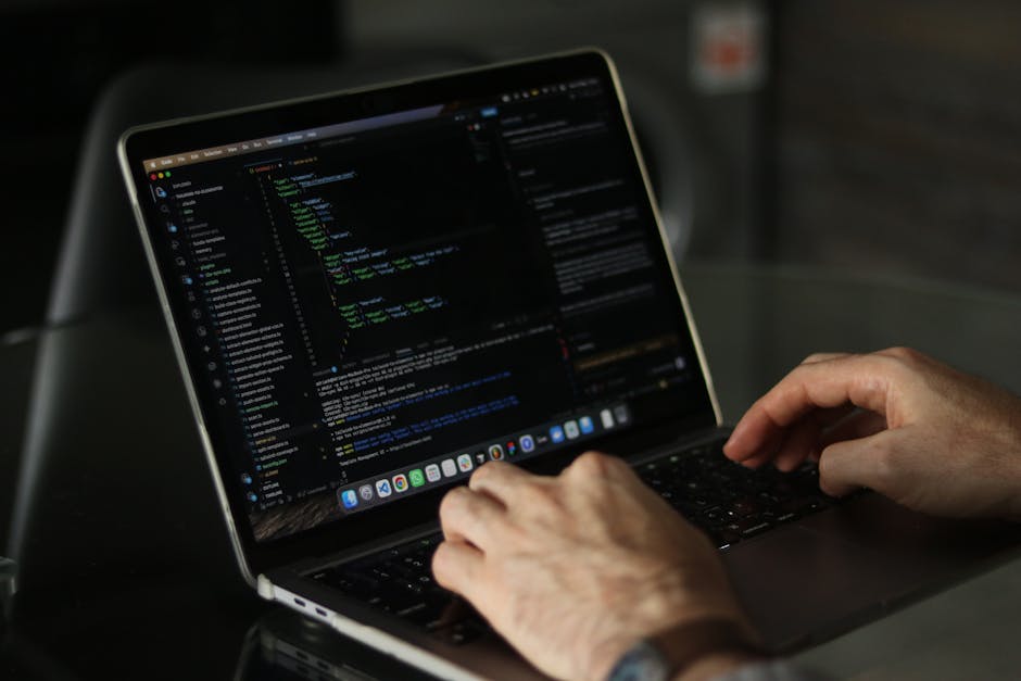 A close-up view of a laptop resting on a wooden table in an indoor setting, displaying lines of code on its screen with a light background and dark text. The laptop has a metallic finish and a black k